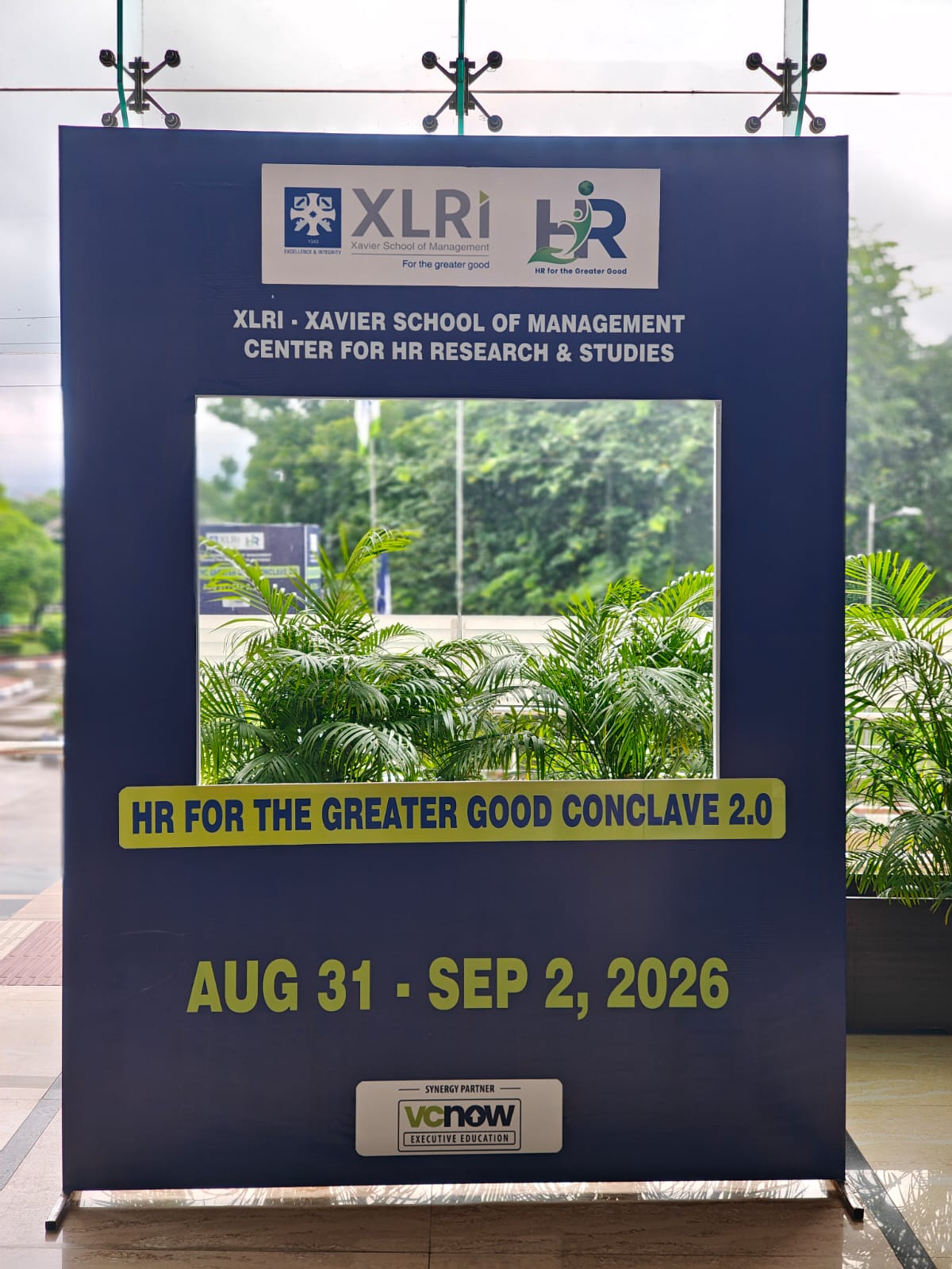 HR for the Greater Good Conclave 2.0 event signage at XLRI featuring the dates August 31 to September 2, 2026 and the VCNow Executive Education synergy partner logo